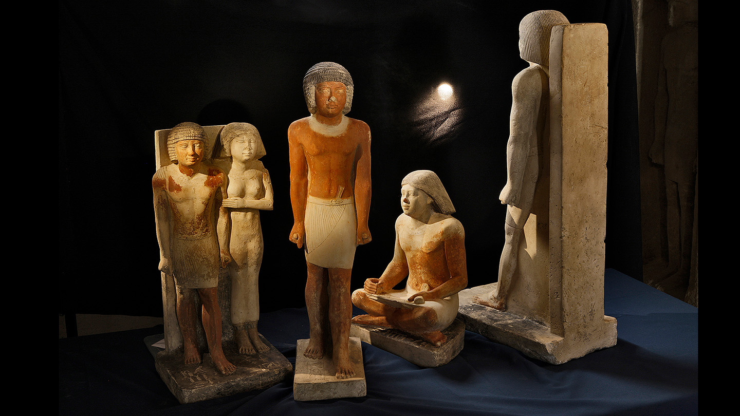 A series of stone statues on a dark background depicting an ancient Egyptian scribe.